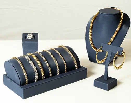 Display of gold and silver jewelry on dark blue stands, featuring bracelets, a necklace, hoop earrings, and a diamond ring.
